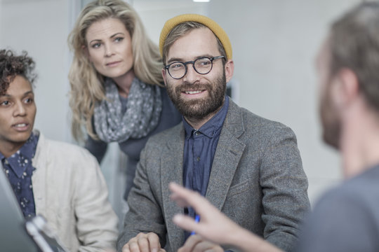 Man with glasses and yellow beanie in meeting with colleagues