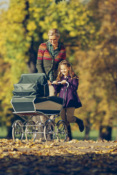 Little girl and her mother pushing a baby carriage in autumnal park