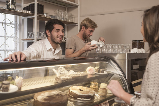 Young woman choosing cake from cake counter in coffee shop
