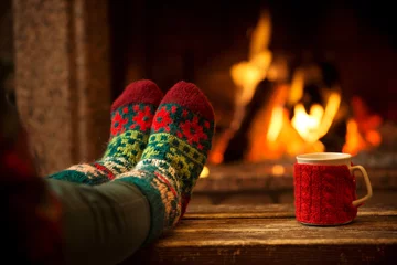 Fotobehang Voeten in wollen sokken bij de kersthaard. Vrouw ontspant bij warm vuur met een kop warme drank en warmt haar voeten op in wollen sokken. Close-up op voeten. Winter en kerstvakantie concept. © AlexMaster