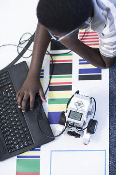 Schoolboy with laptop in robotics class testing vehicle on test track