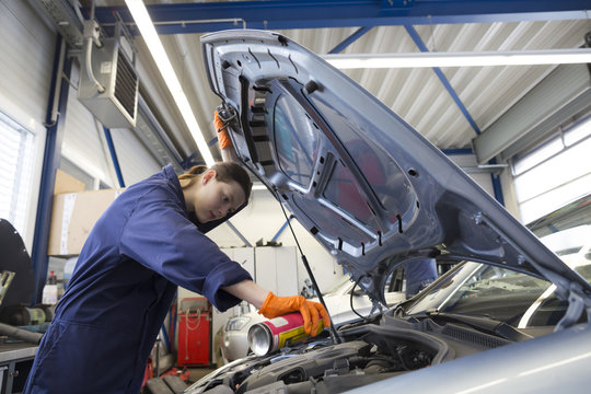 Young woman working in repair garage, checking engine