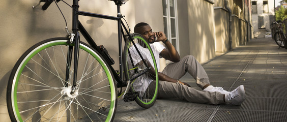 Man sitting on the ground beside his bicycle telephoning with smartphone
