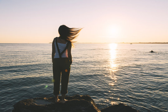 France, Pornichet, woman with blowing hair standing at seafront watching sunset