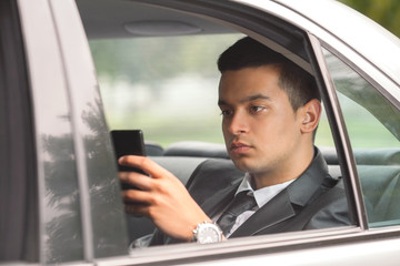 Young businessman using phone while traveling to work by car