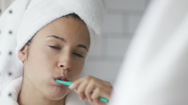 4K Woman with white towel wrapped on her hair brushes her teeth in the mirror, shot on Red Epic Dragon