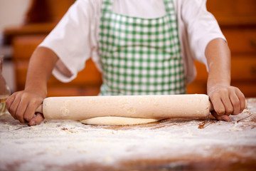 hands of a young boy who pulls the dough in the kitchen