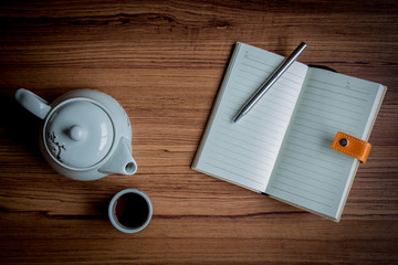 Workplace with a cup of tea, kettle ,notebook and pen on rustic wood background