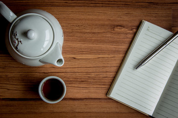 Workplace with a cup of tea, kettle ,notebook and pen on rustic wood background