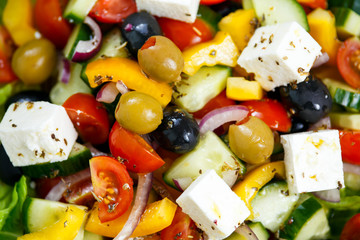 Fresh Close up Vegetable Greek Salad with Feta cheese, black and green olives, cherry tomatoes, yellow pepper, red onion, cucumber. On wooden table.