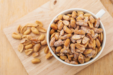 Peanut in a white bowl and spilling out of a bowl on wooden