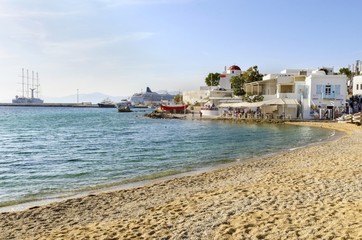 The coastline of Chora in Mykonos, Greece. Typical greek island whitewashed houses on the shore and seaview golden sand promenade overlooking the Aegean sea and calm clean blue water.