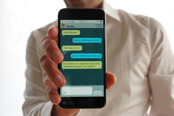 La main d'un homme en chemise blanche tient un smartphone avec une discussion par SMS