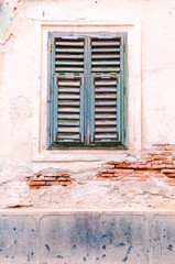 Fototapeta na wymiar Old pale blue slatted window in a brick wall with the white washed rendering eroded in parts.
