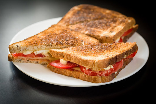 Toasted ham and cheese sandwich on white plate on black background