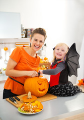 Mother with halloween dressed daughter carving Jack-O-Lantern