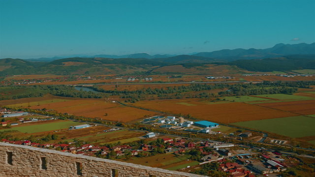 A panoramic view of the Romanian town of Deva from the Old Citadel, showing the town center, crop fields and hills.

