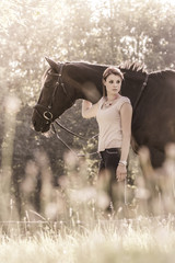 Vintage young equestrian woman with horse in summer sun nature. Scene of a teenager horsewoman holding her best animal friend in a lovely sunny outdoor scene. Vintage portrait format with copyspace
