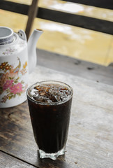Glass of Thai iced coffee with chinese teapot on wooden table. Common drink of Thai street food