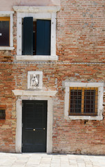 Medieval facade of the old building in Venice with brick wall, bas relief and shutters