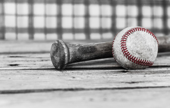 horizontal image of black and white with selective color of a baseball and bat on a wood surface with a checkered background with room for text.

