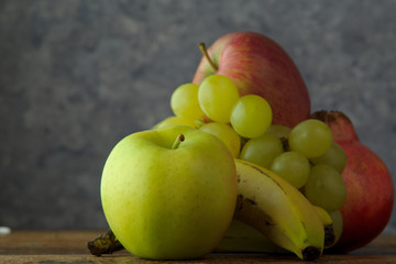 Frutta fresca di stagione, banane, mele, uva e melograno in primo piano sfondo marmo