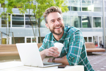 Fototapeta premium Handsome man sitting outdoors with laptop and coffee