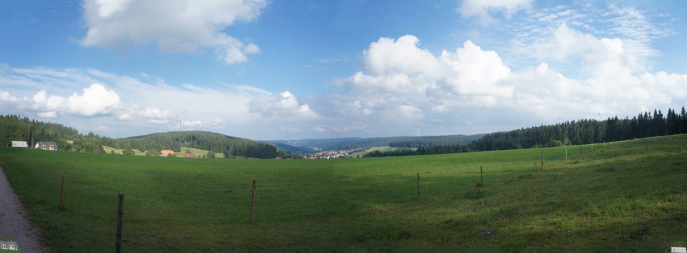 Schwarzwaldpanorama/Landschaft im Schwarzwald in Deutschland; Panoramablick &uuml;ber W&auml;lder und Wiesen, Berge und T&auml;ler, im Tal eine Kleinstadt, blauer Himmel mit wei&szlig;en Wolken,  