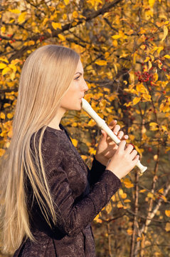 Beautiful young blonde woman playing flute recorder in autumn forest