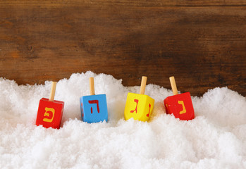 image of jewish holiday Hanukkah with wooden colorful dreidels (spinning top) and chocolate traditional coins over december snow
