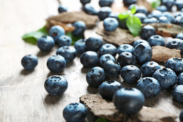 Tasty ripe blueberries with green leaves on wooden table close up