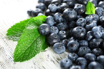 Tasty ripe blueberries with green leaves on wooden table close up