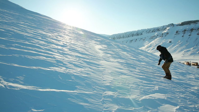 A man trying to climb the mountain on a slippery frozen snow, slips and falls.