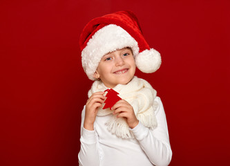 winter, child,  christmas concept - happy girl in santa hat show fir tree wool toy on red