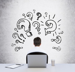 Rear view of a sitting person at the working desk who is looking for the best solution of the...