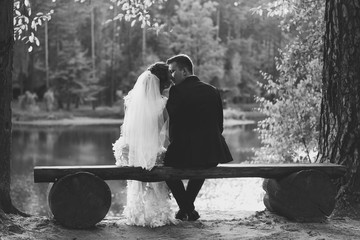 Monochrome photo of bride and groom kissing on bench at riverban