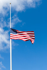 American flag flying at half mast against blue sky with white clouds. Copy space