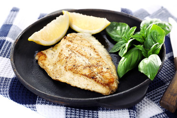 Dish of fish fillet with basil and lemon on table close up