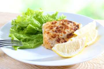 Dish of fish fillet with lettuce and lemon on table close up