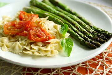 Roasted asparagus and tasty pasta with vegetables on plate on wooden table background
