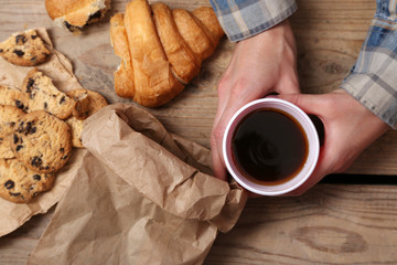 Female hands holding cup of coffee and cookies on wooden table close up