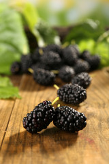 Heap of ripe mulberries with green leaves on table close up