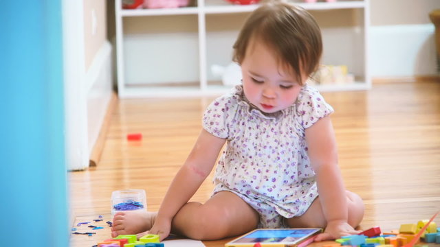 Happy toddler girl enjoying watching her tablet computer inside her house