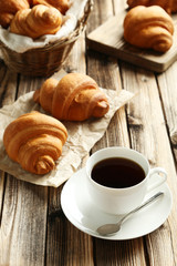 Tasty croissants with cup of coffee on brown wooden background