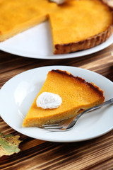 Tasty pumpkin pie on plate on a brown wooden table