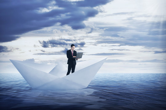 Asian Business Man Working With Laptop On The Paper Boat