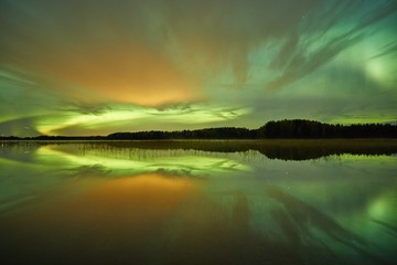 Northern lights and night clouds on the night sky. The water of a lake reflects the green light of...