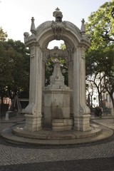 Fototapeta na wymiar Largo do Carmo fountain in Lisbon, in front of the ruins of the convent, surrounded by trees