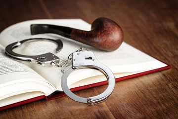 Obraz premium handcuffs and pipe over an open book
