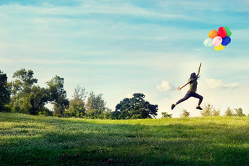  woman running and jumping touch balloons floating in the sky on green grass and flower field  